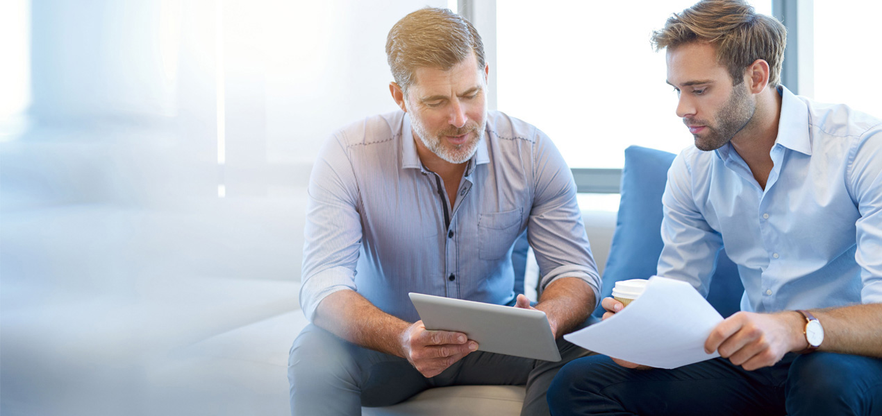 Mature businessman using a digital tablet to discuss information with a younger colleague.