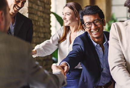 Meeting of people talking, with two men smiling while shaking hands
