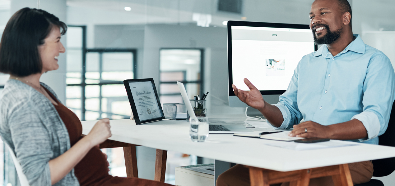 A man and woman collaborate at a desk, looking at a computer screen in a modern workspace.